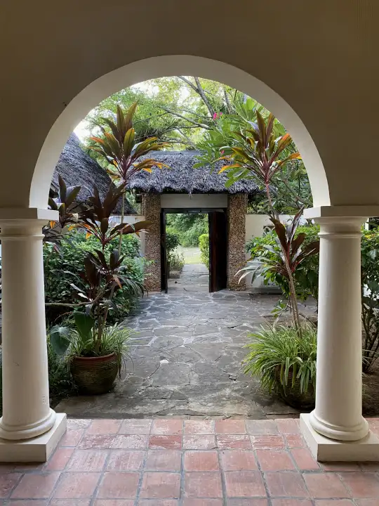 Arched veranda opening onto a stone path and carved gate through the tropical garden