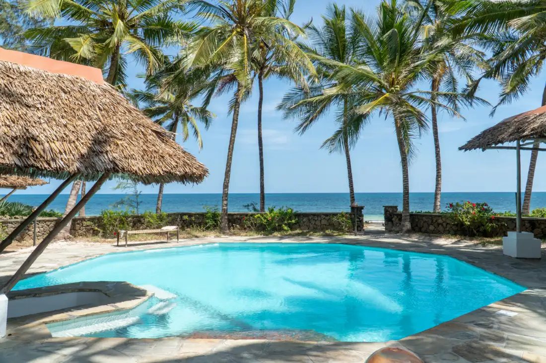 Pool deck with thatched shades and coconut palms facing the Indian Ocean