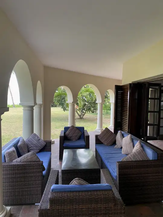 Shaded veranda lounge with rattan sofas behind Swahili arches overlooking the lawn