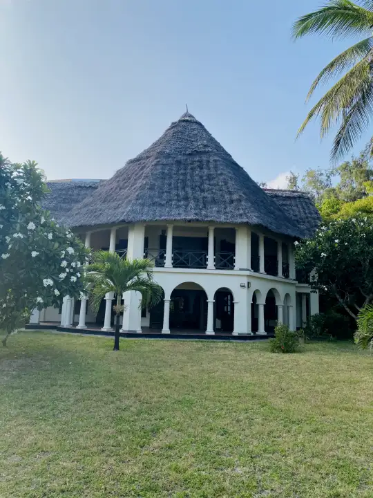 The two-storey makuti-roofed villa framed by flowering frangipani trees